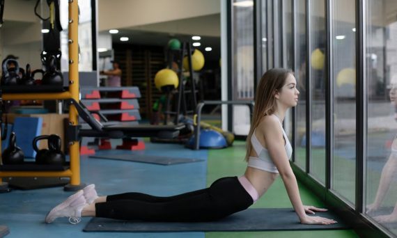 A young woman in yoga attire performs a cobra stretch in a well-equipped gym.